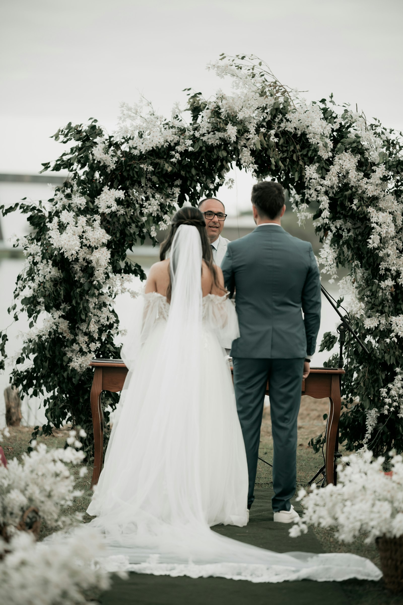 Novios de espalda frente a un arco de flores blancas