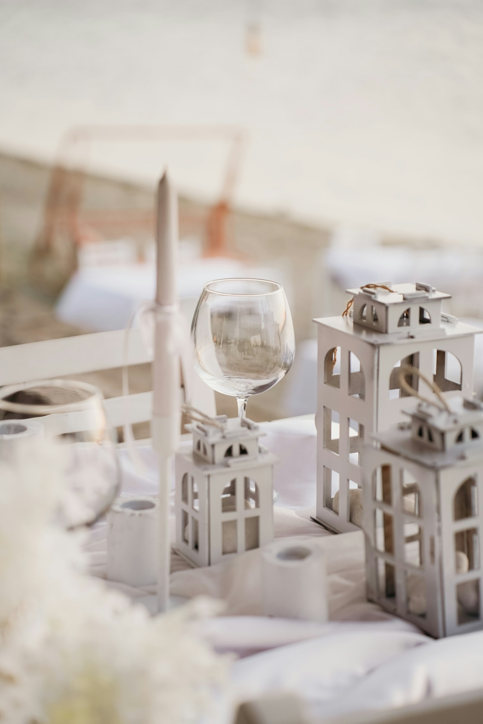 Velas blancas altas junto a copas sobre una mesa blanca